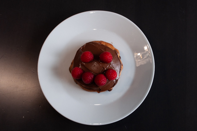 A one-person portion cake with chocolate on top and raspberries.
