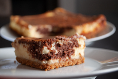 A baked cheesecake that was made for a photography class. It’s cut and the piece is in front of the rest of the cake.